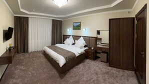 Ein Hotelzimmer mit einem großen Bett, einem Schreibtisch, einem Sessel, einem Fernseher und einem Kleiderschrank.