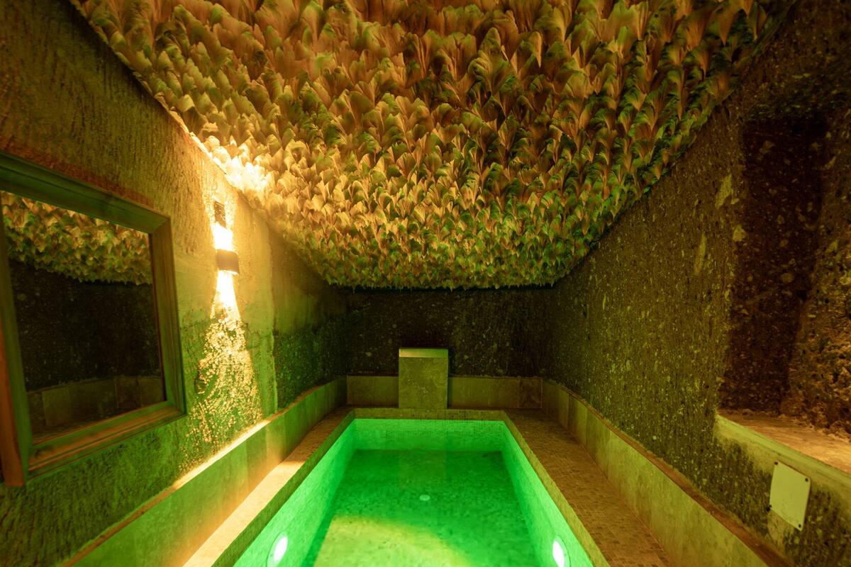 A swimming pool with green lighting, surrounded by stone walls and a textured ceiling.