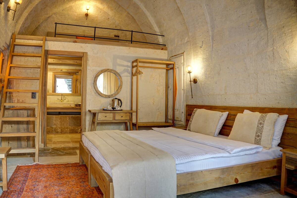 A rustic bedroom with a wooden bed, a ladder, a small desk, and a mirror.