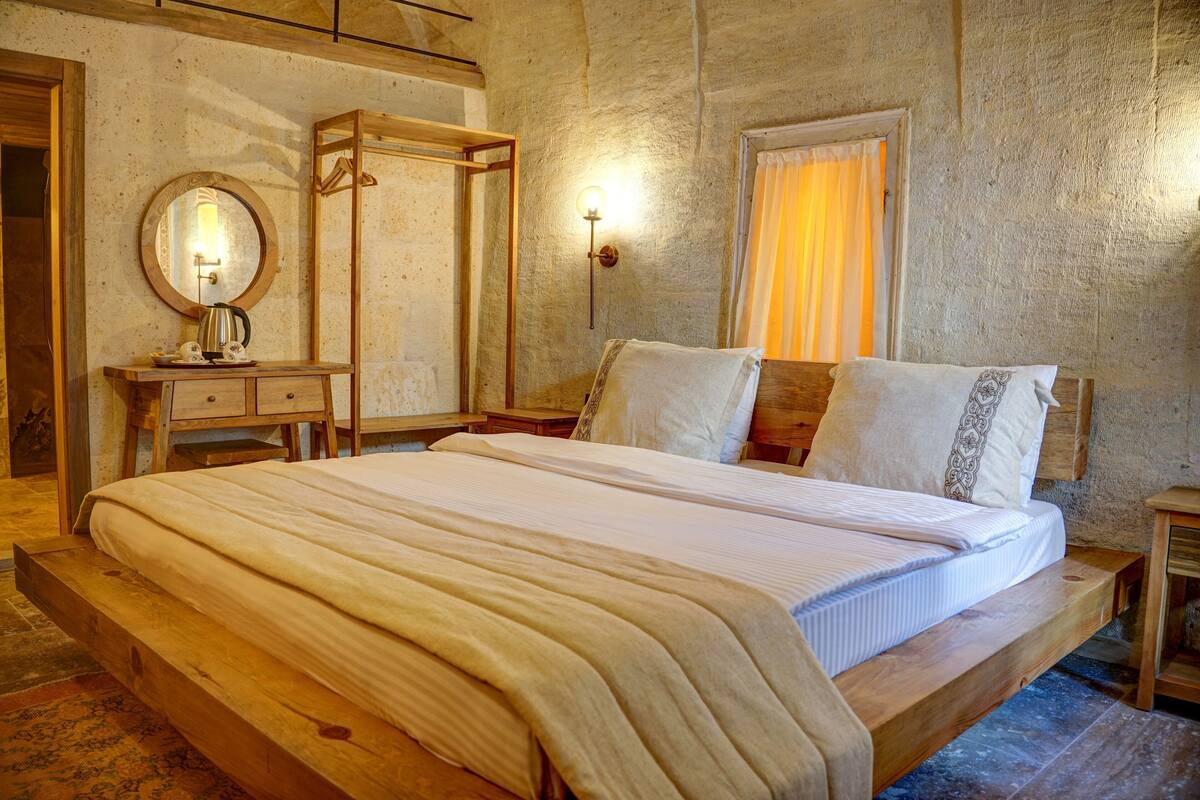 A bedroom with a wooden bed, a bedside table, a mirror, and a wall-mounted light fixture.