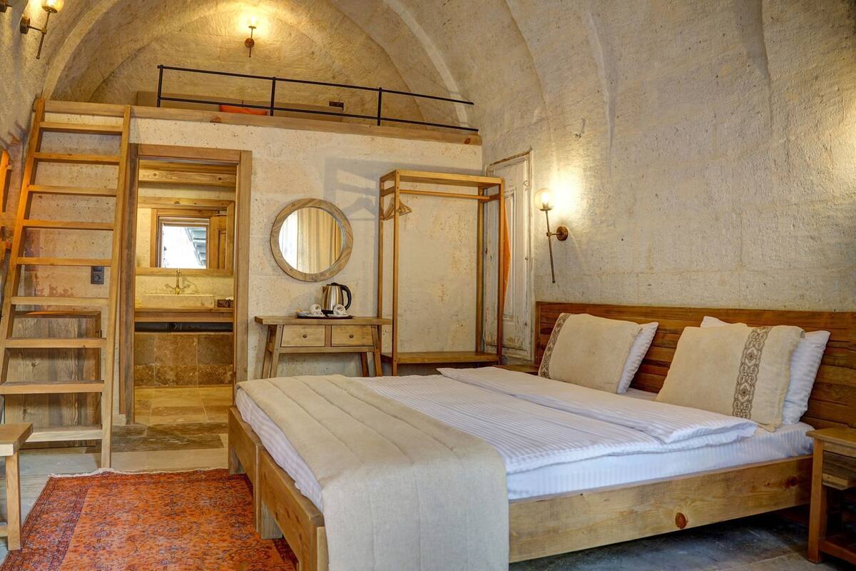 A rustic bedroom with a wooden bed, a ladder, a small desk, a mirror, and a wardrobe.