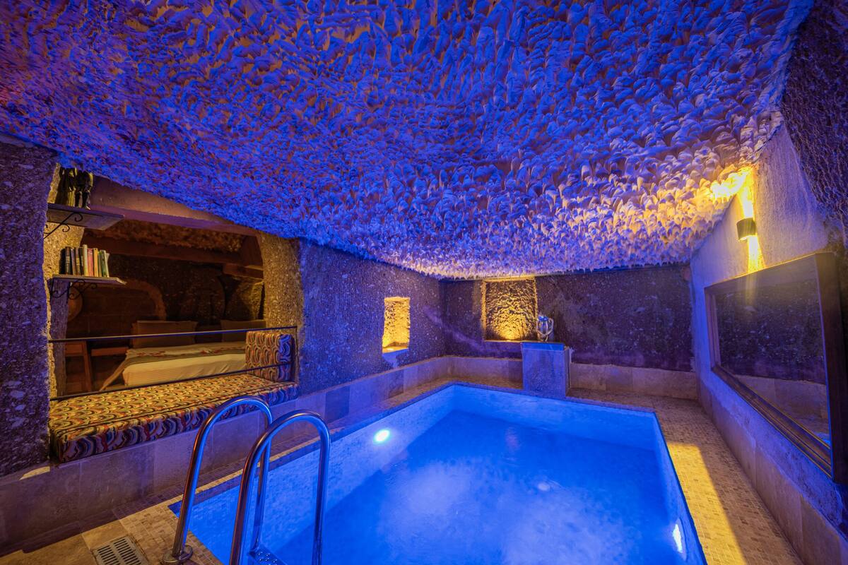 A spa room with a stone ceiling, a pool, and a seating area with books.