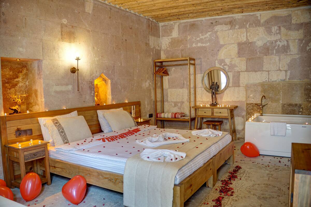 A wooden bed with rose petals, a wooden nightstand, a mirror, a vanity with a sink, and a bathtub.