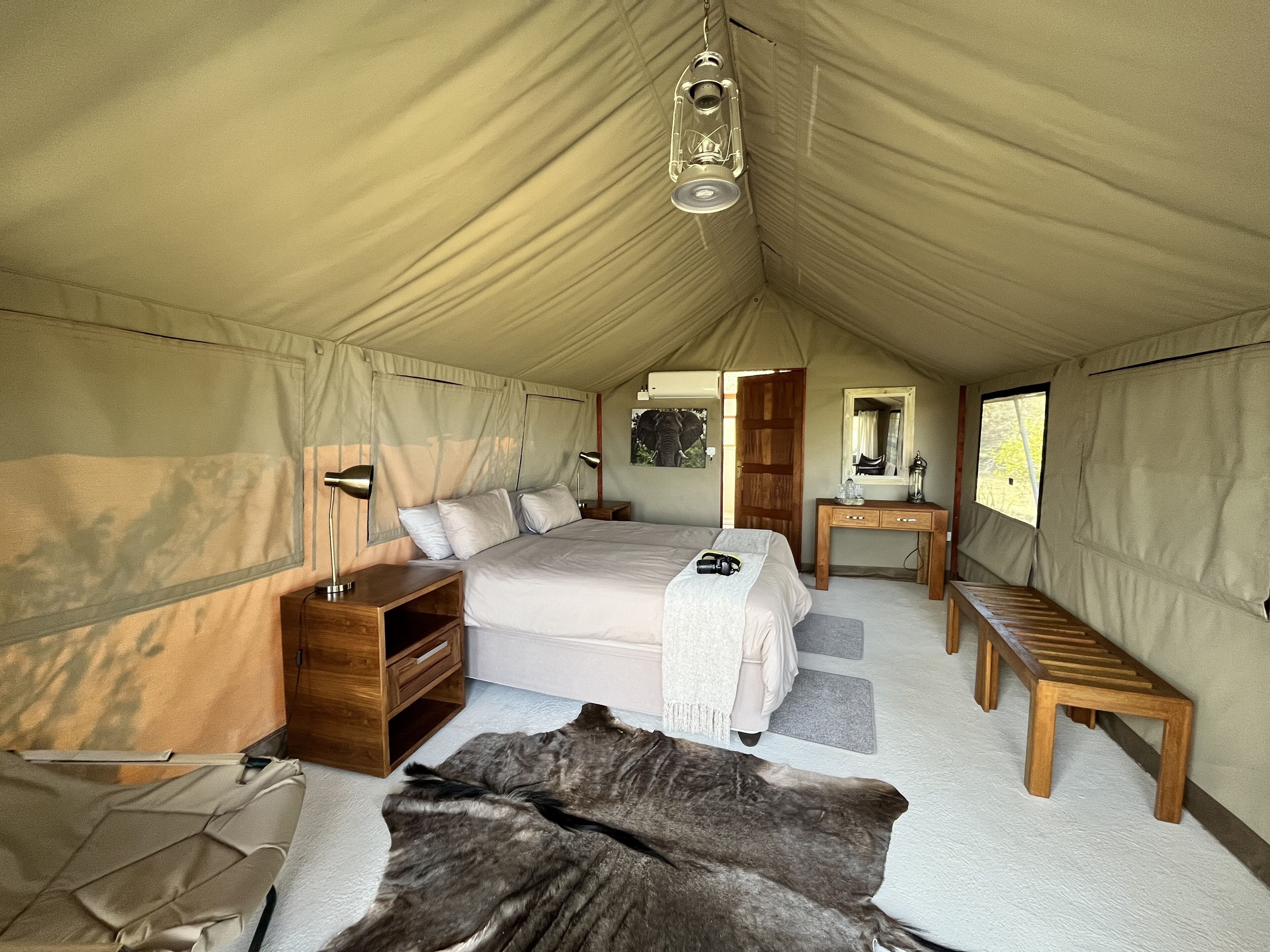 Een tent met een bed, een houten bureau en een spiegel.