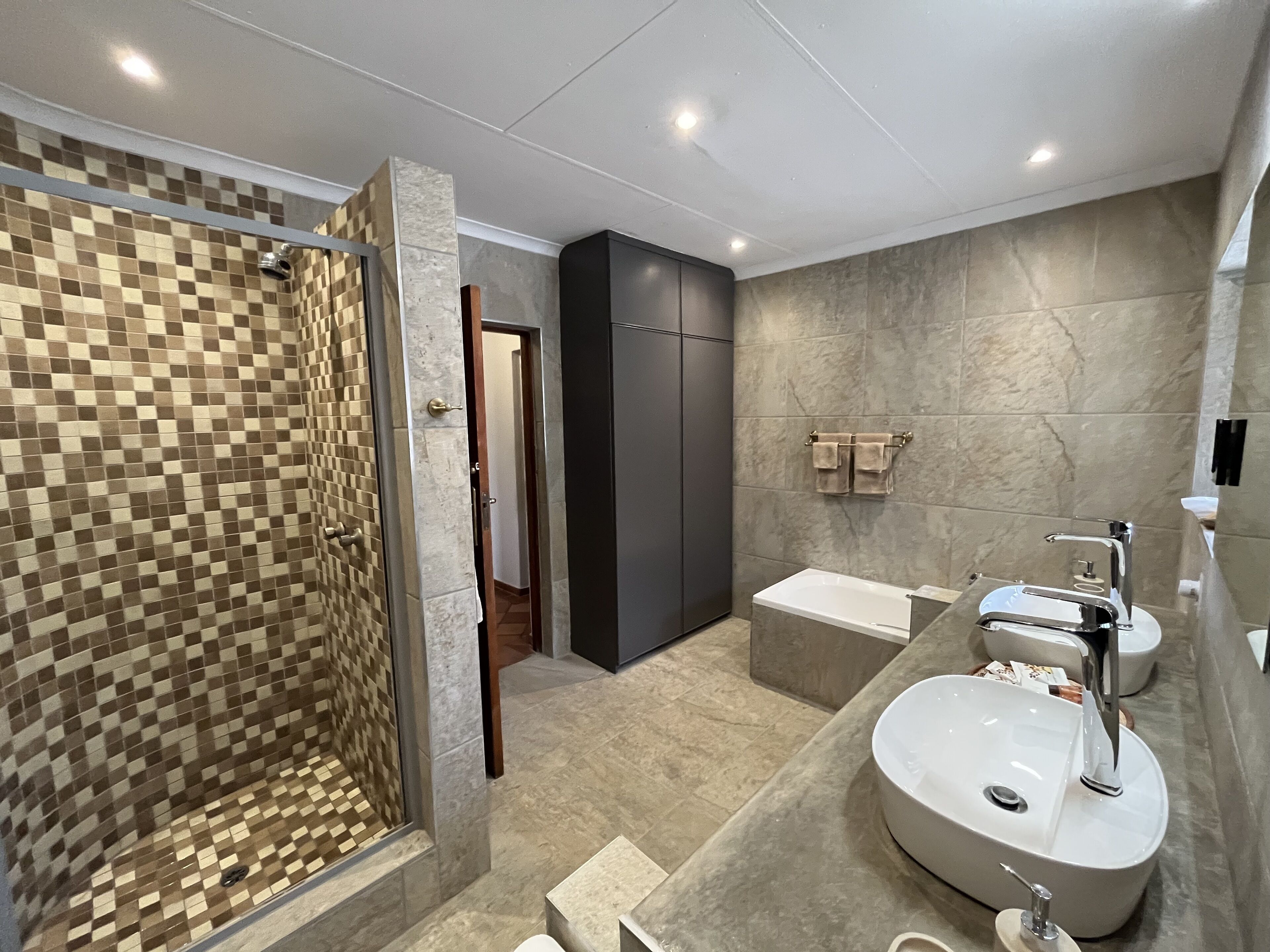 Un baño moderno con ducha acristalada, una bañera grande y un tocador con dos lavamanos.