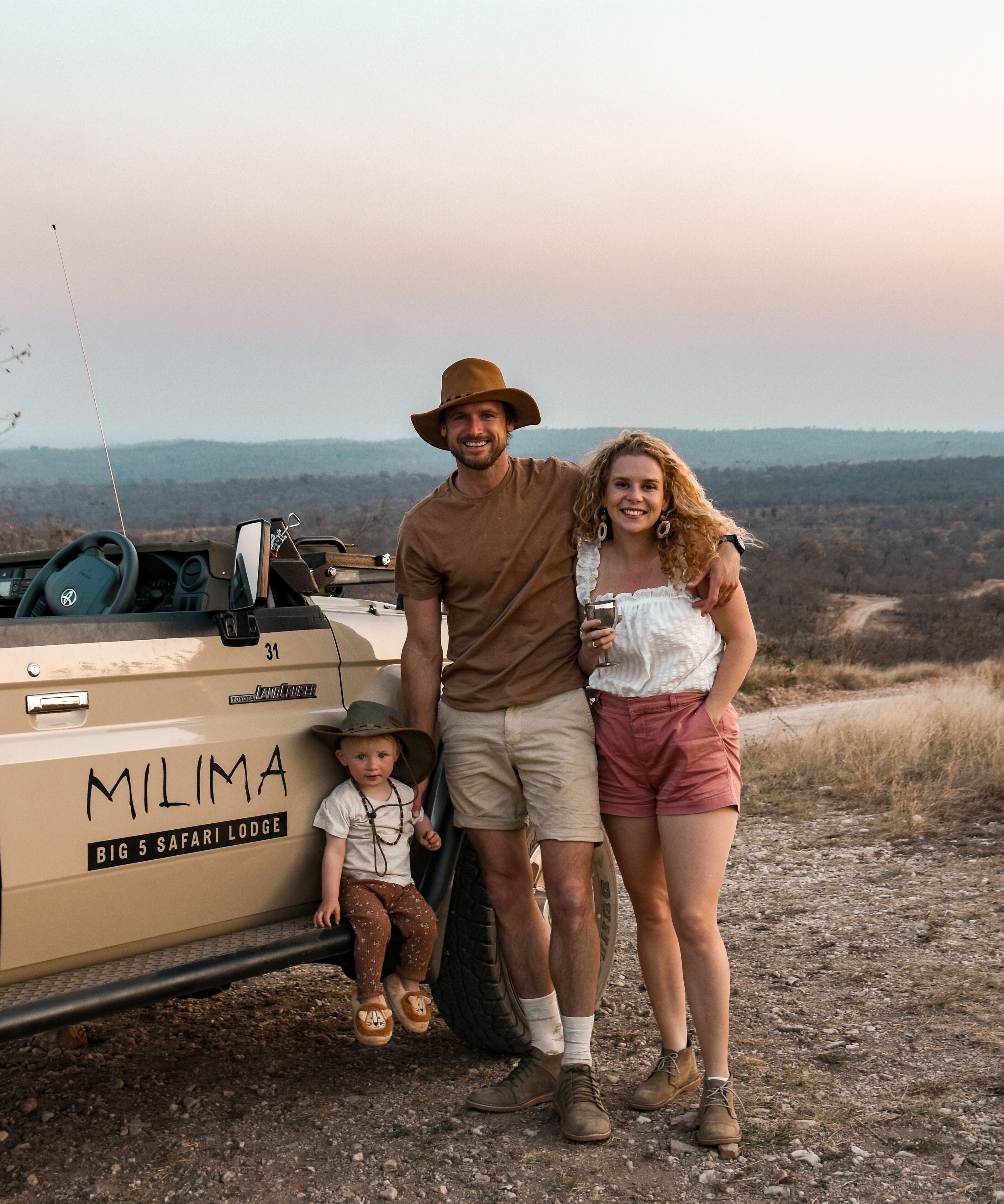 A family of three standing next to a safari vehicle with the text "MILIMA BIG 5 SAFARI LODGE" on the side.