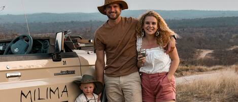Una familia de tres personas de pie junto a un vehículo de safari, con el texto "MILIMA BIG 5 SAFARI LODGE" en el lateral.