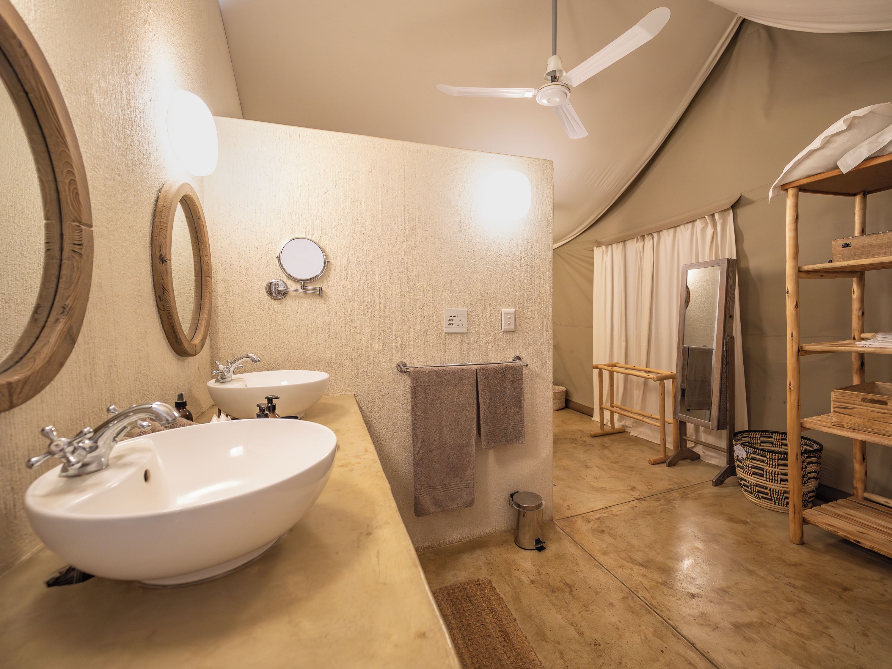 A bathroom with a large sink, two mirrors, a ceiling fan, and a wooden shelf.