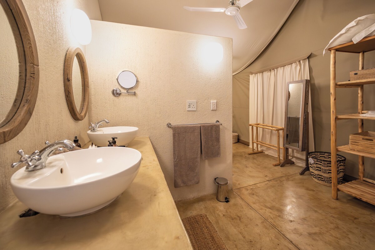 A bathroom with a large sink, two mirrors, a ceiling fan, and a wooden shelf.