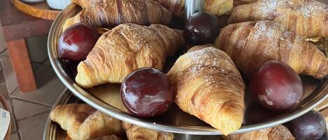 A multi-tiered display of pastries and fruits, including croissants and plums, on a metal stand.