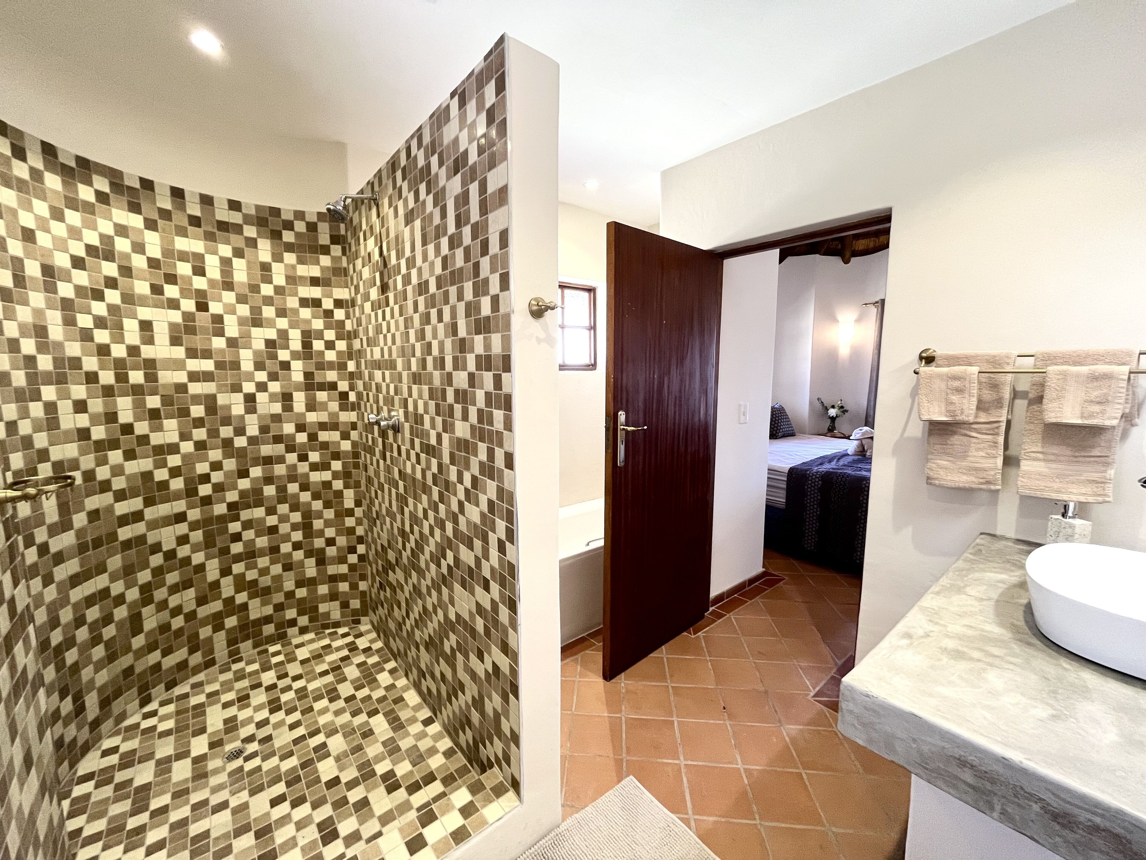 Een badkamer met een betegelde douche, een houten deur, een bed en een wastafel met handdoeken.