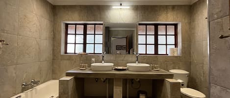 A modern bathroom with a bathtub, two sinks, and a toilet.