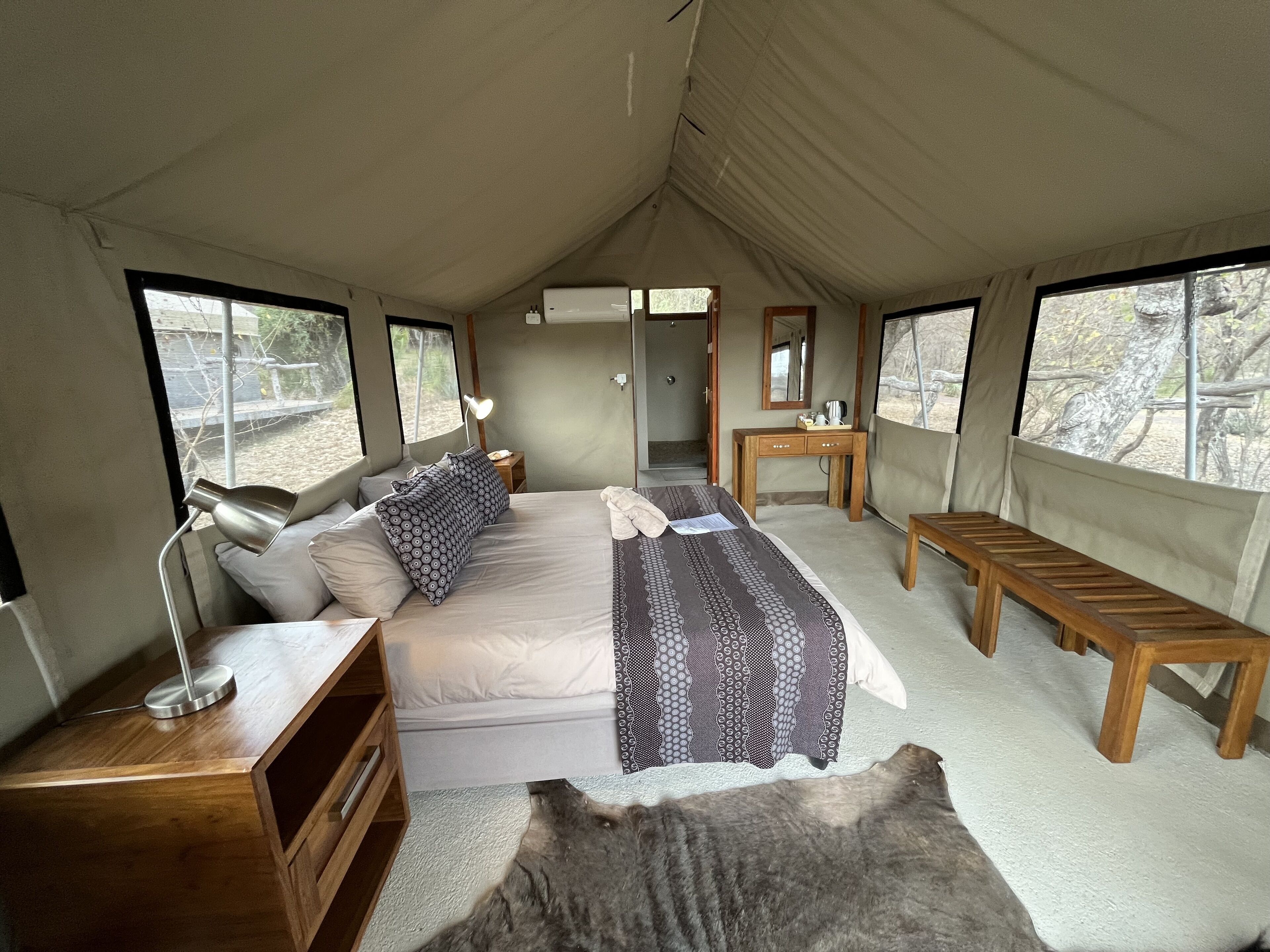 Una tenda arredata con un letto, un comodino, una lampada, una panca di legno e un tavolino con uno specchio.