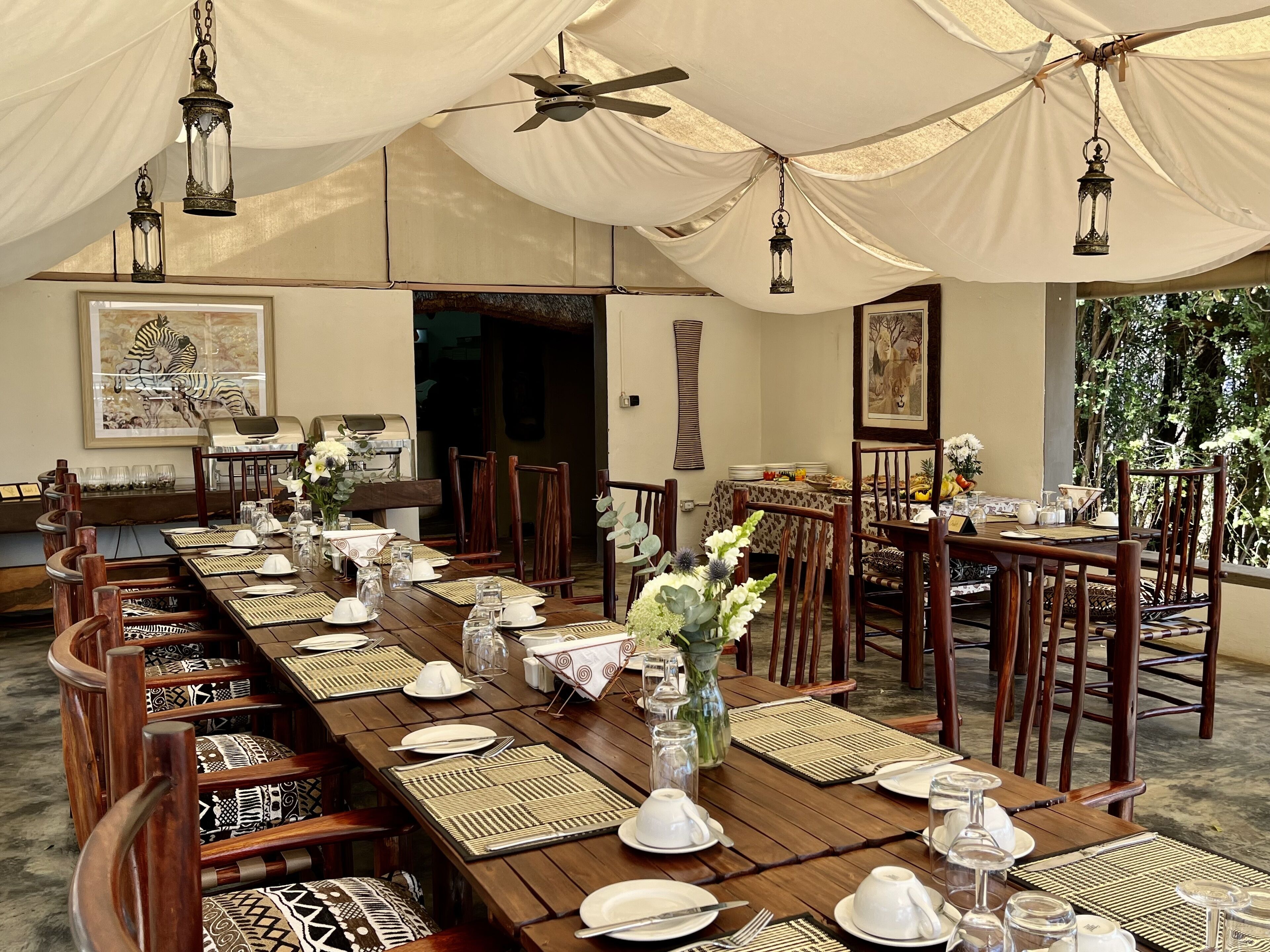 Un área de comedor con carpas, mesas de madera dispuestas para una comida, rodeada de sillas.