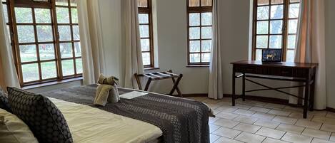 A hotel room with a bed, a desk, and a laptop. There are windows with curtains, an air conditioning unit, and a security camera.