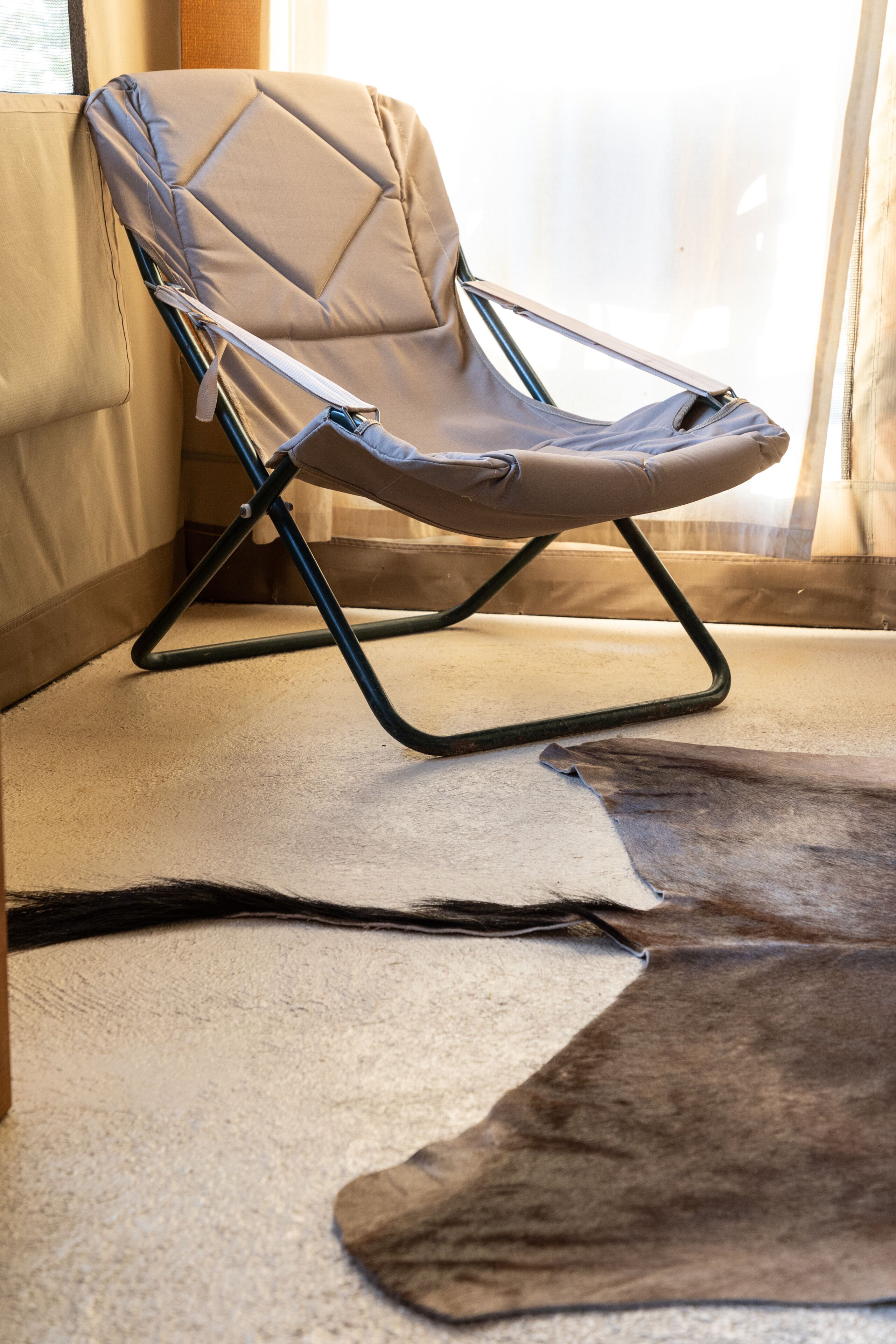 Une chaise dotée d’un dossier rembourré et d’une structure en métal, placée sur un sol recouvert d’une moquette, à côté d’une fenêtre ornée de rideaux légers.