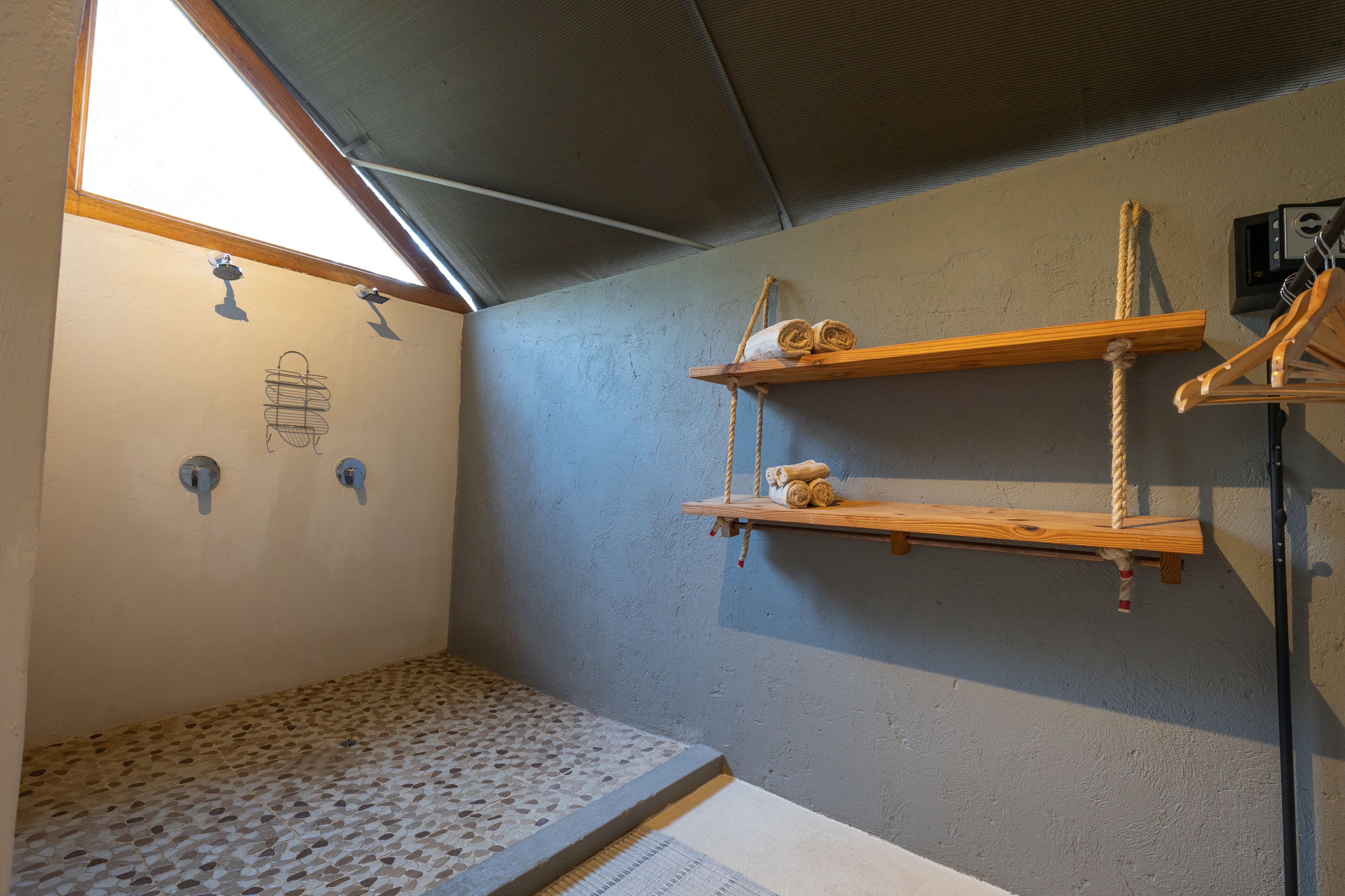 Une salle de bain avec un sol carrelé, un espace douche et des étagères en bois où sont rangées les serviettes.