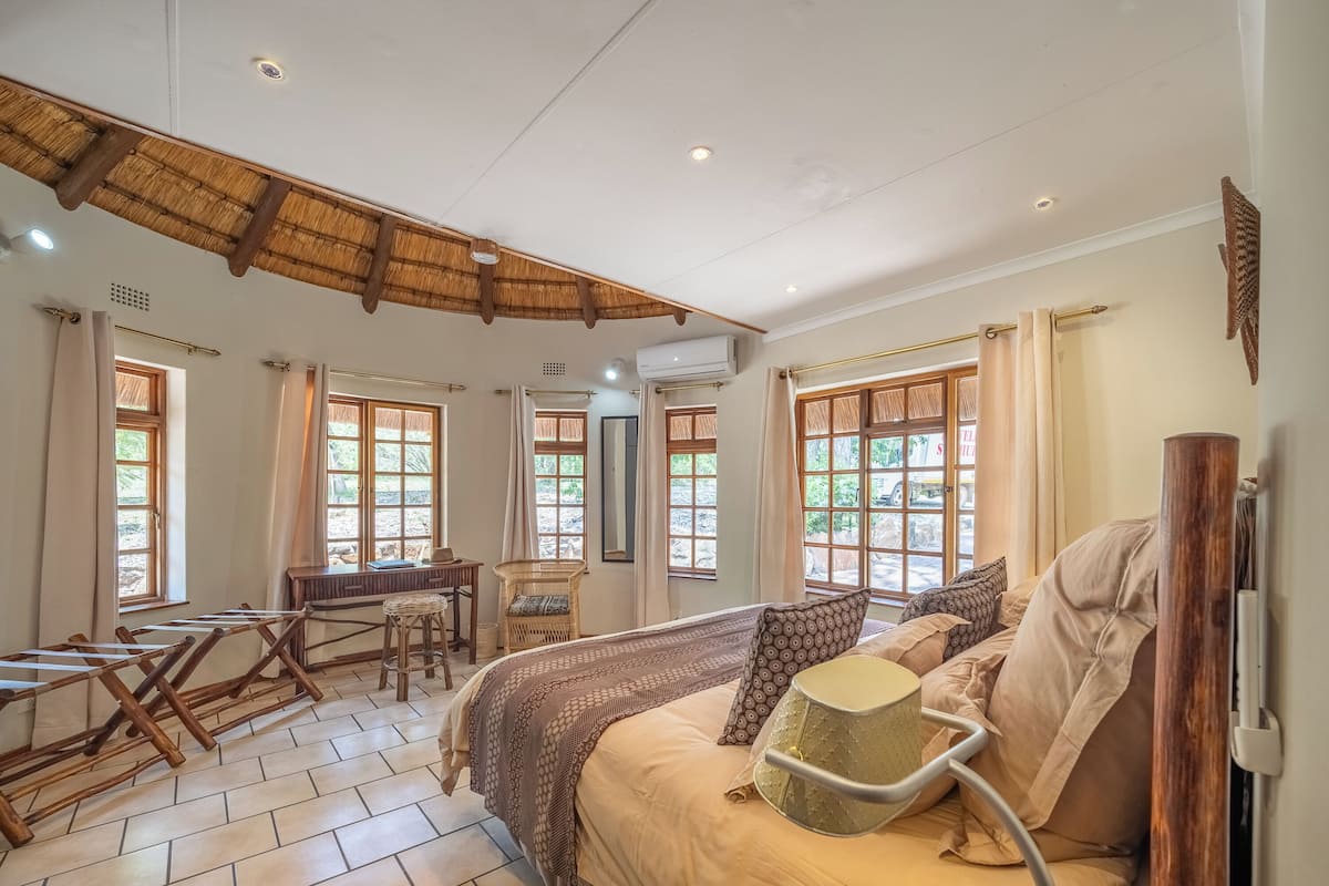 A room with a bed, a desk, and a chair. There are windows with curtains.