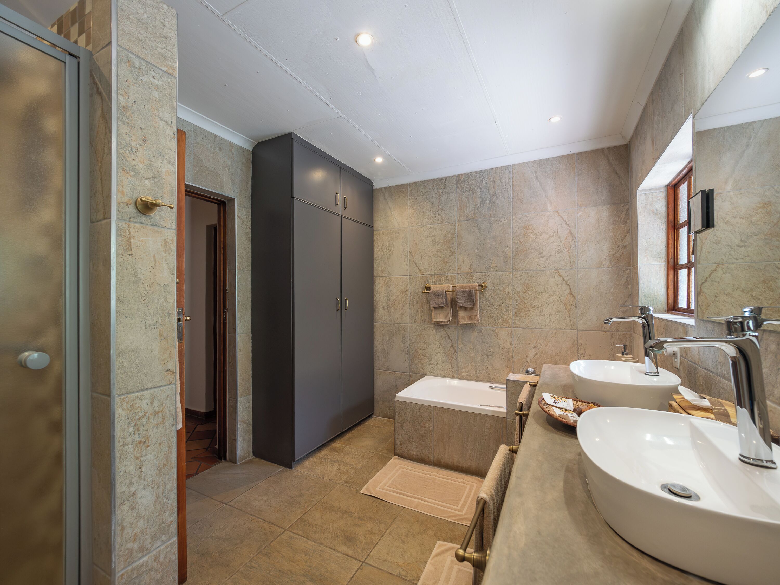 A modern bathroom with a bathtub, two sinks, and a large mirror.