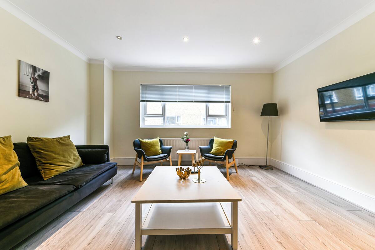 A modern living room with a sofa, two armchairs, a coffee table, a TV, and a window with blinds.