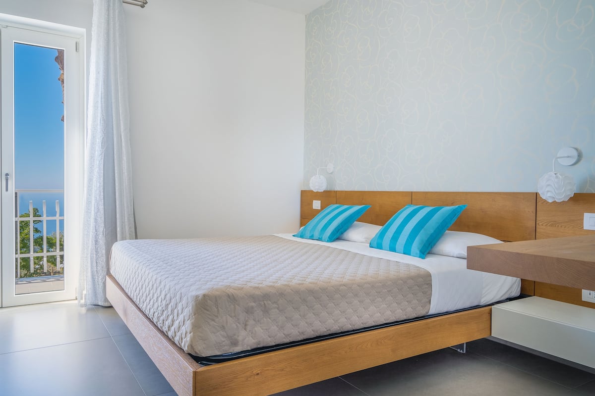 Ein modernes Schlafzimmer mit einem hölzernen Bett, weißer Bettwäsche und blauen Kissen.