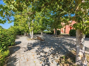 A paved courtyard with a bench, trees, and a building in the background. - Quercia Alta by Interhome (Scarlino)