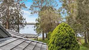 Une vue d’un lac où l’on aperçoit des bateaux, entouré d’arbres et d’une maison avec un toit en pente.