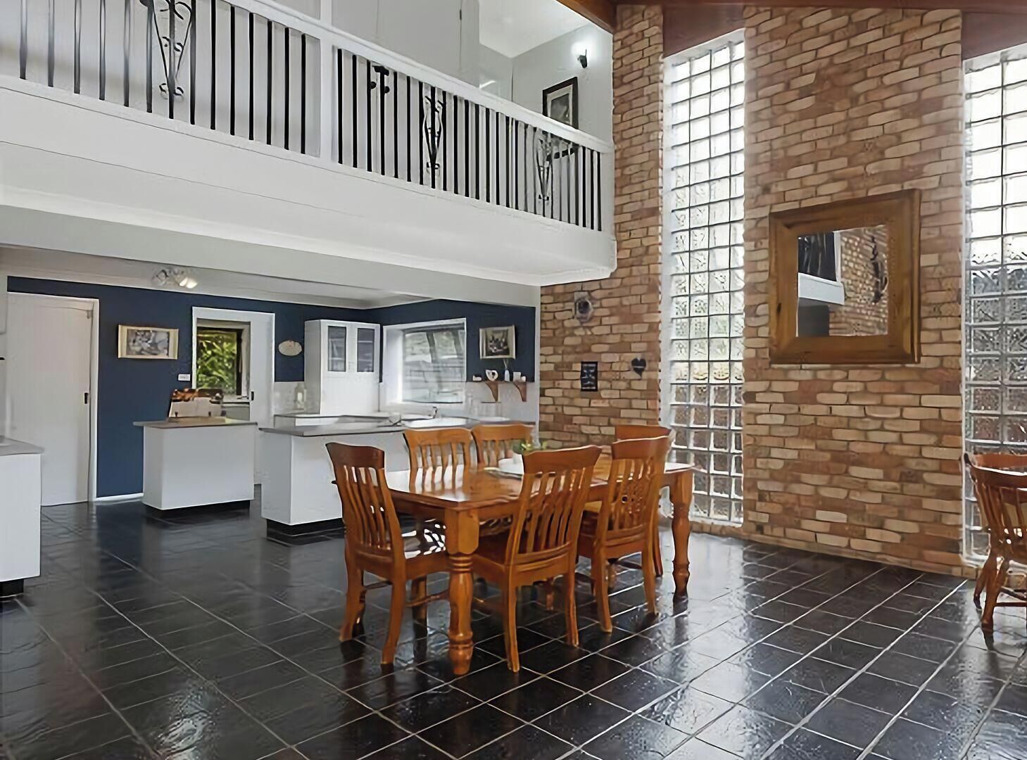 A spacious kitchen with a central island, a dining area with wooden chairs, and a brick wall with a window.