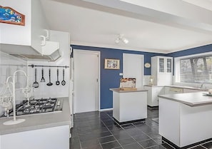 Una cocina moderna con gabinetes blancos, estufa a gas, utensilios colgantes y una ventana con persianas.