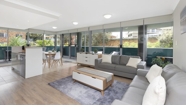 A modern living room with a grey sofa, a coffee table, and a dining area with a table and chairs. - Spacious. Coastal. Fresh. (Forster)