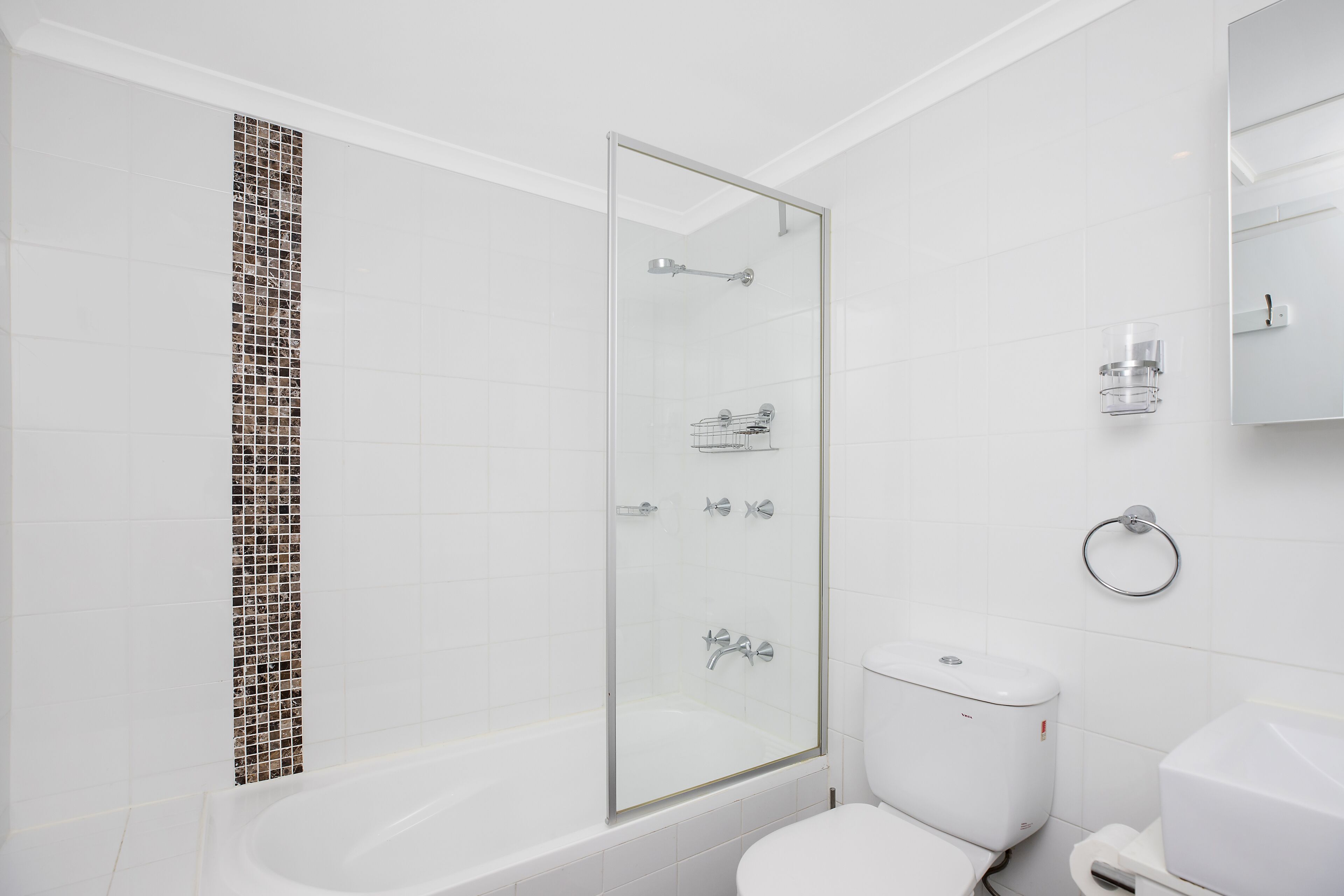 Un bany modern amb dutxa tancada per vidre, un vàter blanc i un lavabo blanc.