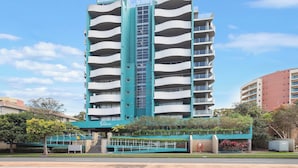 A multi-story hotel with a distinctive teal and white color scheme, featuring balconies on each floor and a central staircase. - Spacious. Coastal. Fresh. (Forster)