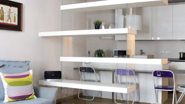 A modern living room with a grey sofa, a small white table, and a kitchen area with white cabinets and a countertop. - Brera Apartments Alla Scala (Milan)