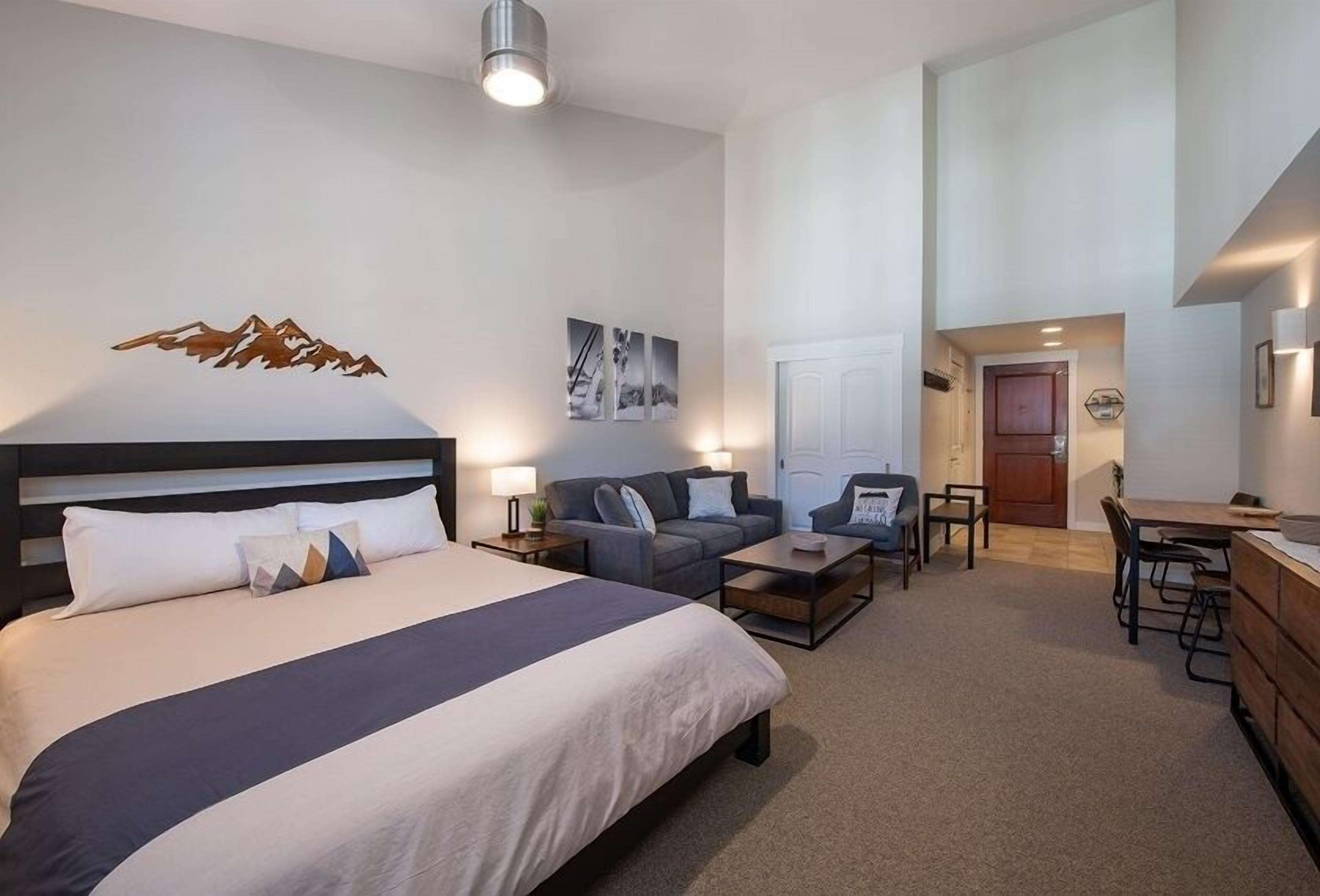A hotel room with a large bed, a sofa, a coffee table, and a desk area.