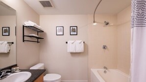A modern bathroom with a sink, toilet, and bathtub. There are towels on a rack and two framed pictures on the wall.