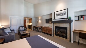 A modern living room with a fireplace, a dining area, and a kitchen visible through an open door.