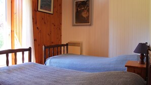 Una habitación con dos camas, paredes de madera, un radiador, una lámpara y dos cuadros enmarcados.
