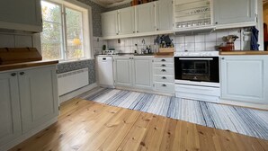 Una cocina con armarios blancos, encimera de madera, horno empotrado y ventana con vistas a árboles.