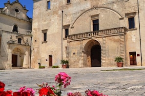 A historic building with a central arched entrance, a bell tower, and potted plants.