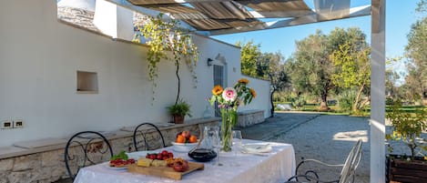 An outdoor dining area with a table set for two, surrounded by stone walls and covered by a pergola.