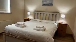 Ein ordentlich bezogenes Bett mit zwei Handtüchern, einem Kopfteil, Nachttischlampen und einem Bild an der Wand.