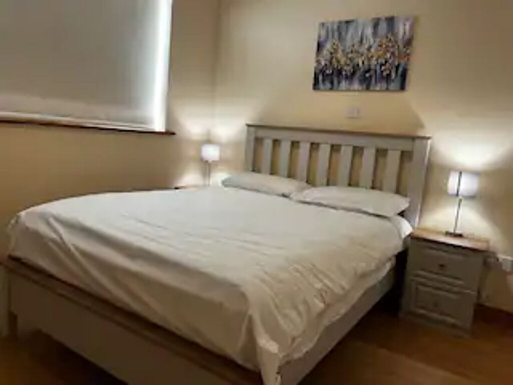 A bedroom with a bed, nightstands, and a painting on the wall.