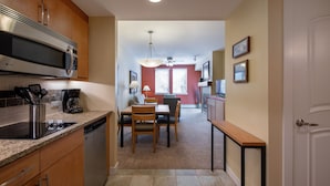 A modern kitchen with stainless steel appliances, a dining area with a table and chairs, and a hallway leading to a living space.