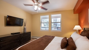 A bedroom with a bed, a TV, a dresser, and a ceiling fan.