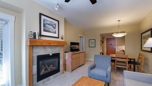 A living room with a fireplace, a television, a dining area with a table and chairs, and a ceiling fan.
