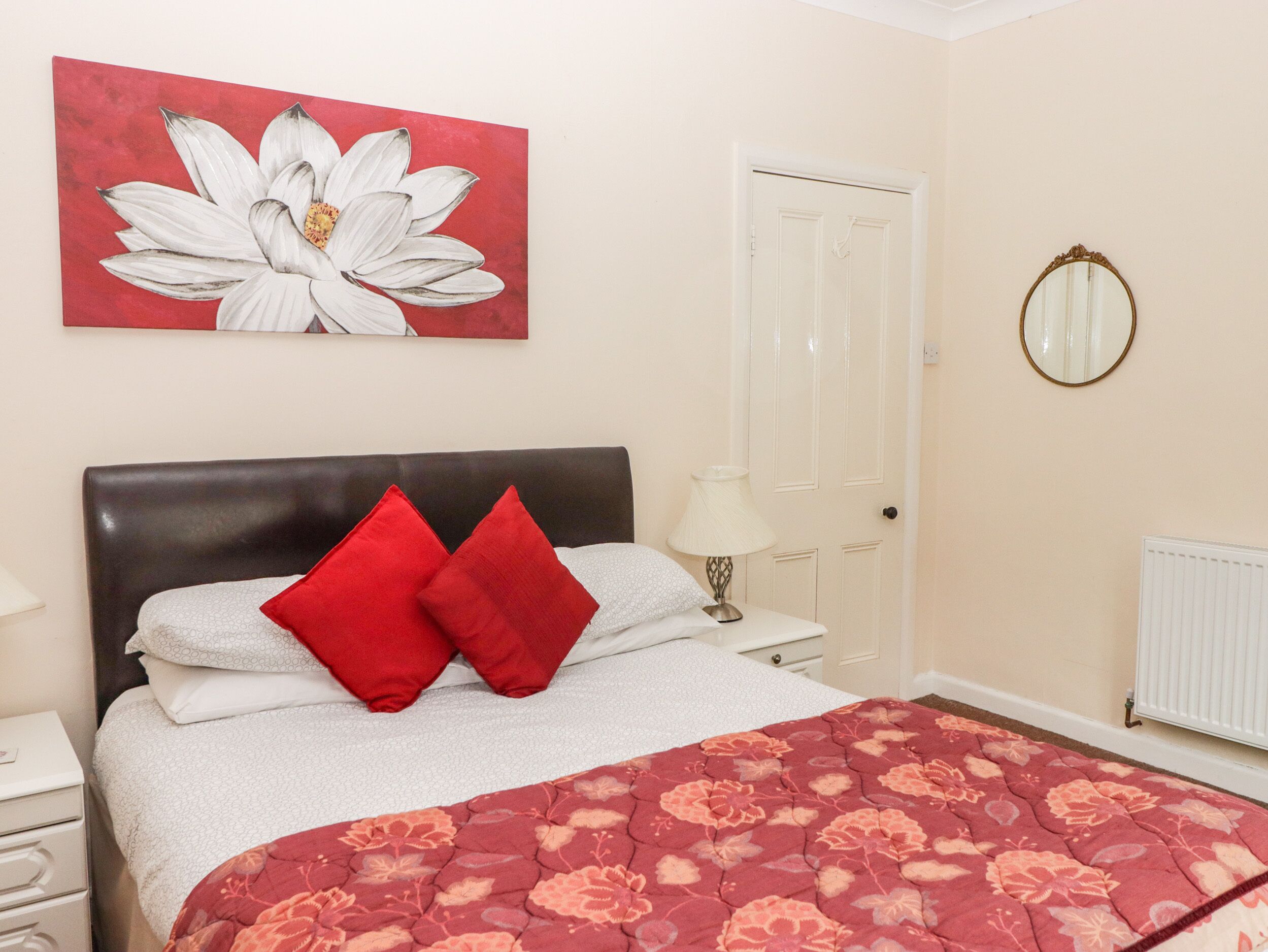 A bedroom with a bed, a nightstand, a lamp, a door, and a mirror.