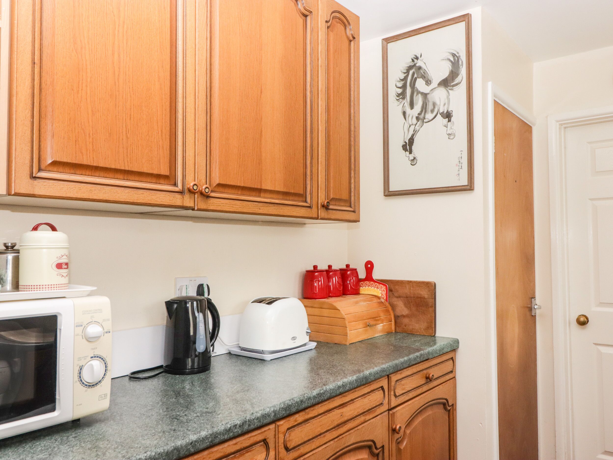 A kitchen with wooden cabinets, a microwave, a toaster, a kettle, and a red kettle set on the counter.