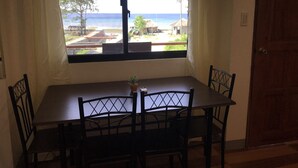 Ett rum med ett bord och fyra stolar, ett fönster med utsikt över stranden och havet samt en dörr.