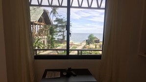 Ett rum med ett bord och två stolar, ett fönster med utsikt över en strand och några byggnader.