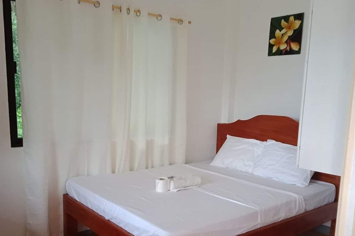 Una cama individual con sábanas blancas en una habitación con suelo de madera y paredes blancas.